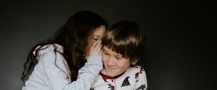 girl in gray jacket whispering on boy's right ear